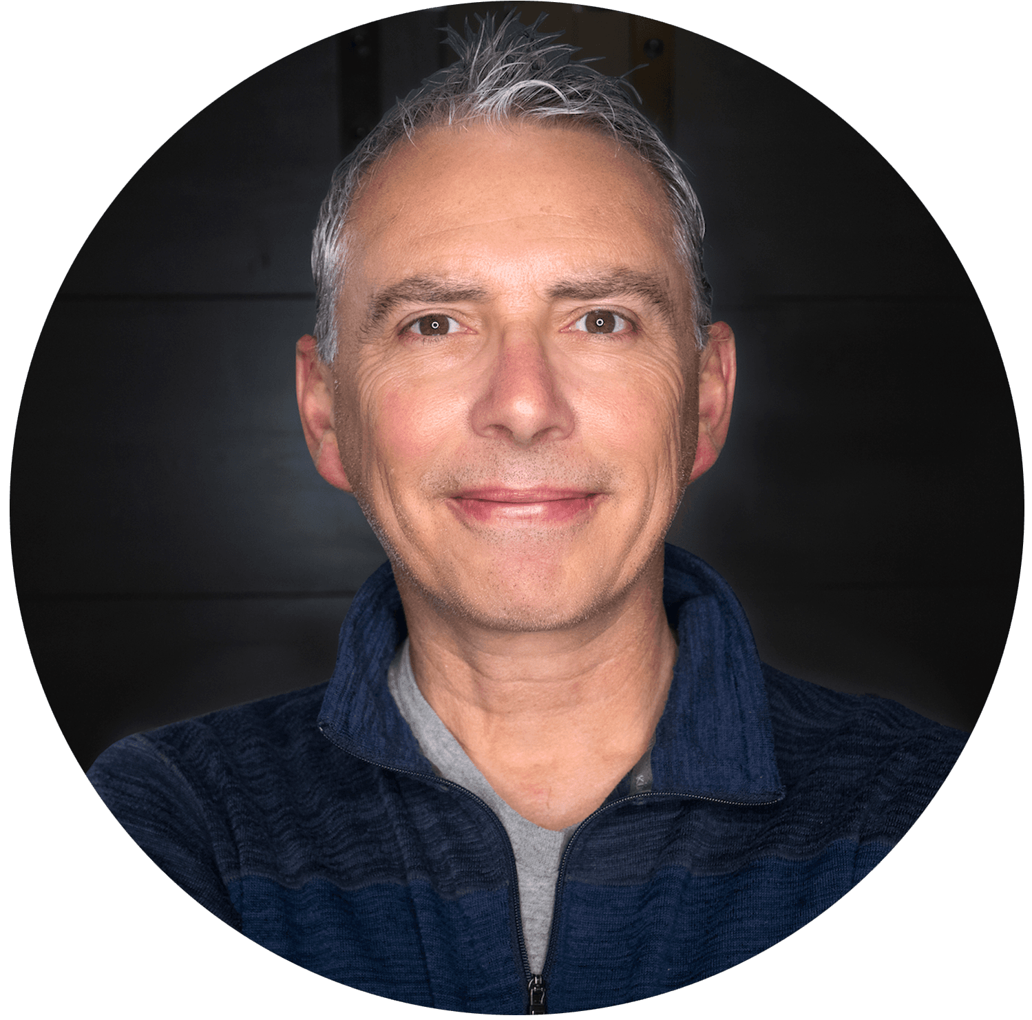 Smiling middle-aged man with spiky grey hair wearing a blue sweater in a circular frame.
