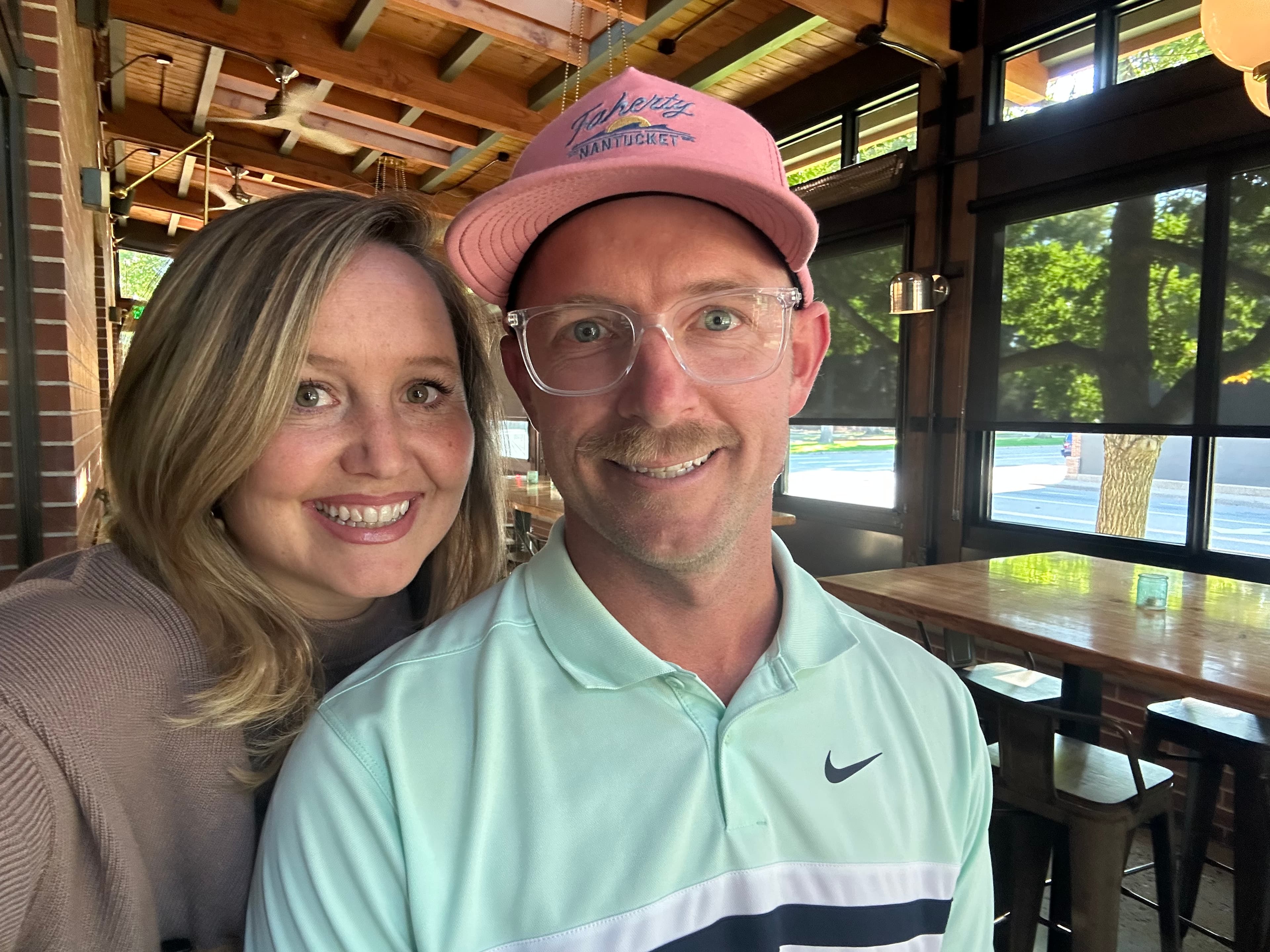 Smiling man in a pink hat and a woman posing together in a rustic restaurant.